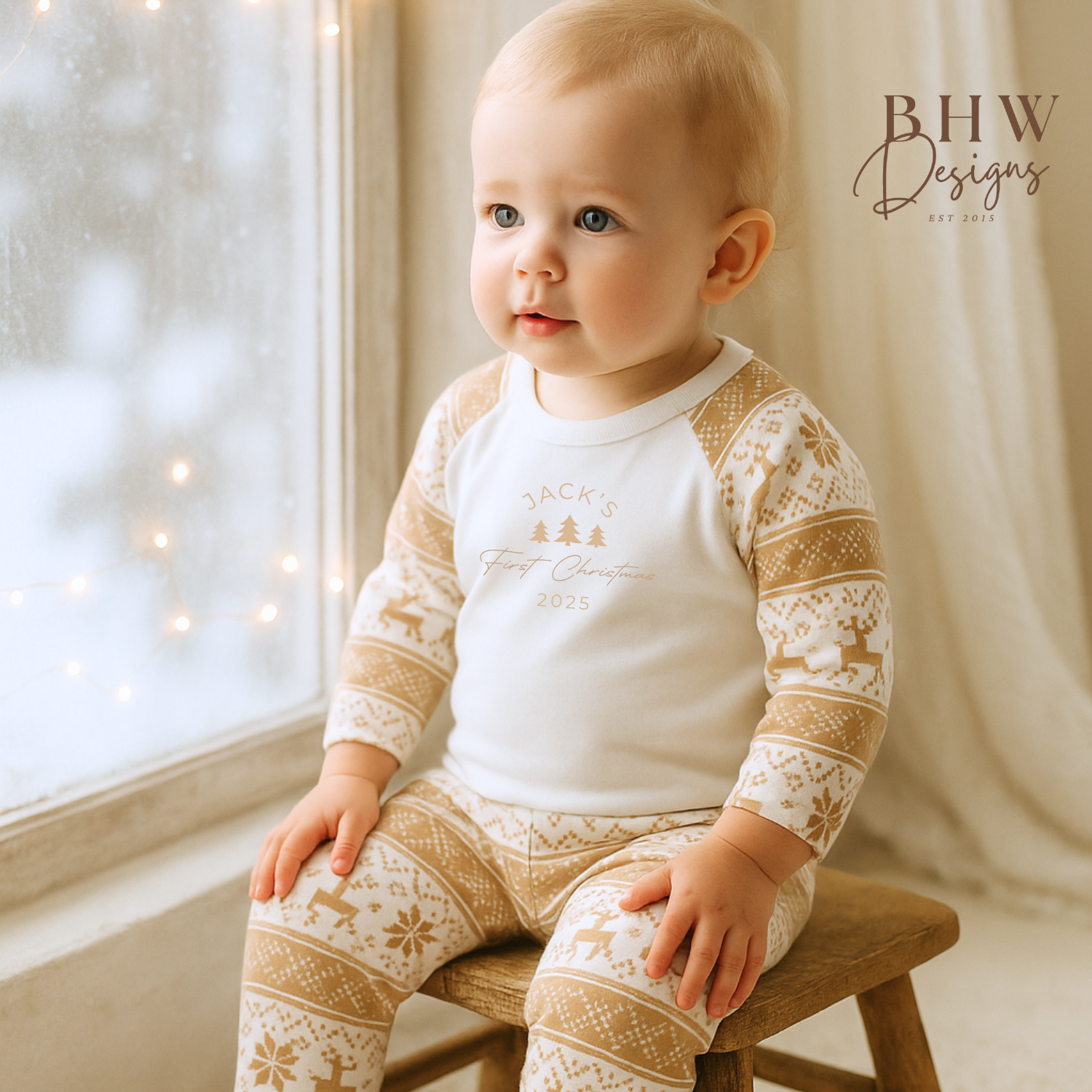 Baby wearing a white and beige fair isle pyjamas with a personalised first Christmas motif on the front.