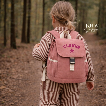 Child wearing a pink backpack with 'Clover' branding in a forest setting