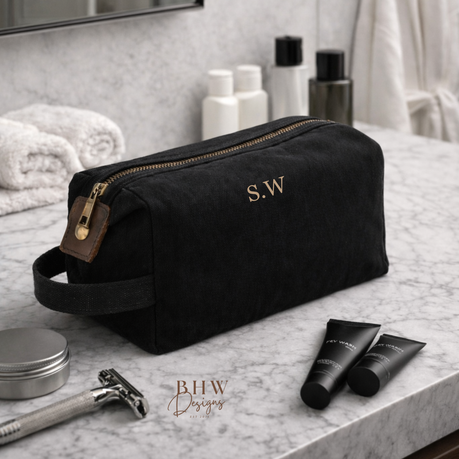 Black toiletry bag with initials on a bathroom counter with grooming products.