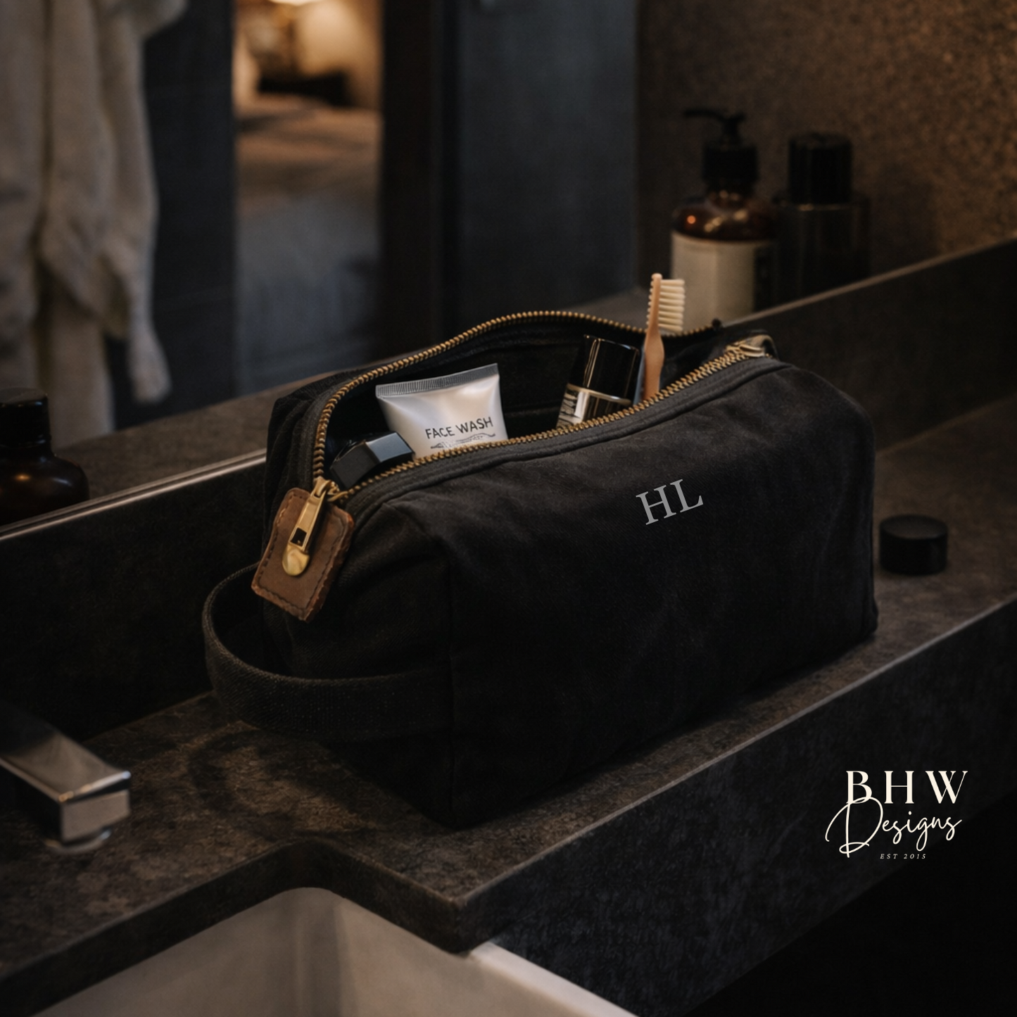 Black toiletry bag with 'HL' initials on a bathroom counter, featuring 'BHW Designs' branding.