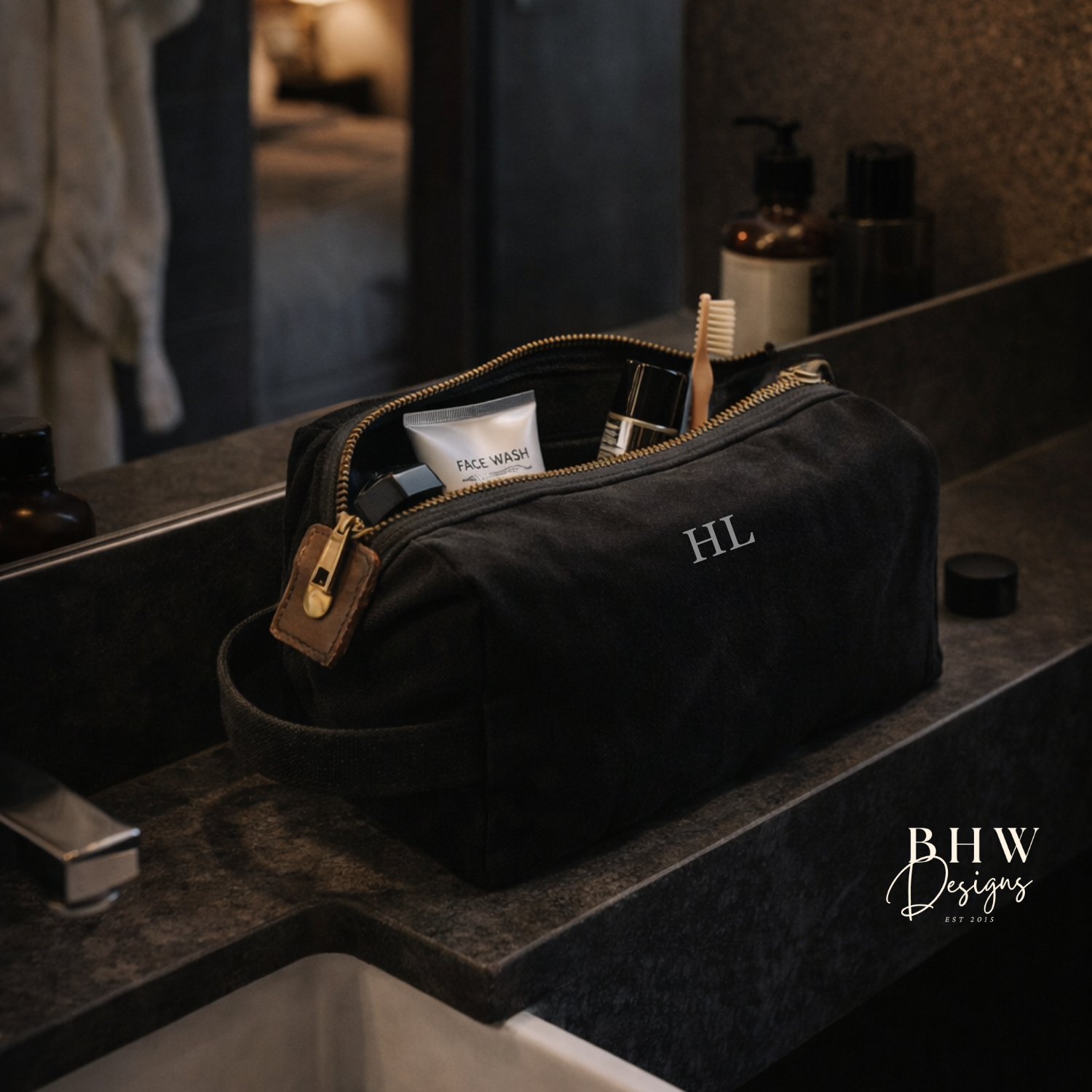 Black toiletry bag with 'HL' initials on a bathroom counter, featuring 'BHW Designs' branding.