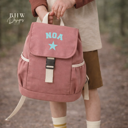 Pink backpack with 'NOA' and a star design, worn by a person in an outdoor setting.