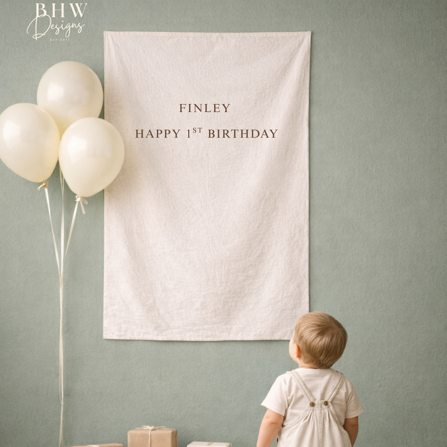 Child looking at a 'Happy 1st Birthday' banner with balloons on a green wall.
