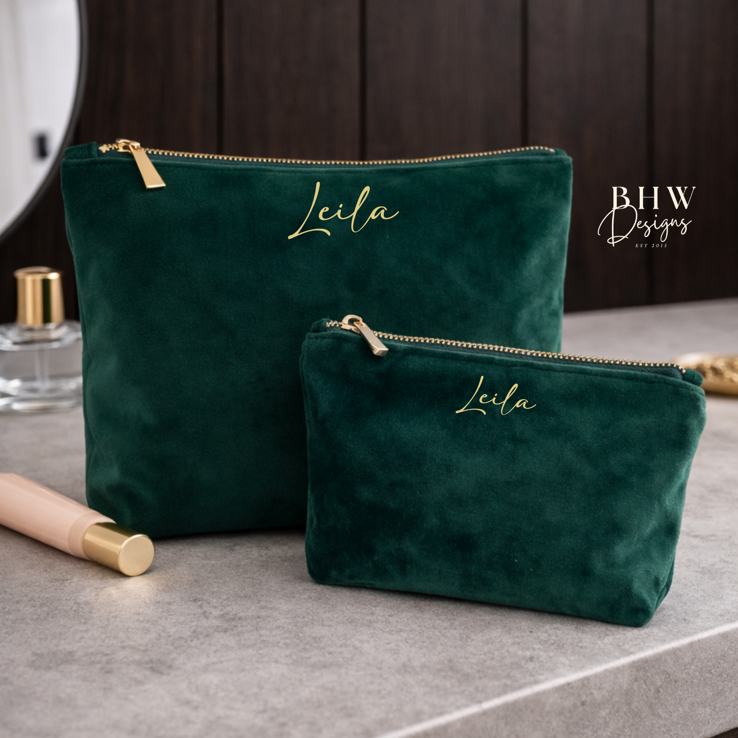 Two green velvet pouches with 'Leila' embroidered on them, placed on a gray surface.