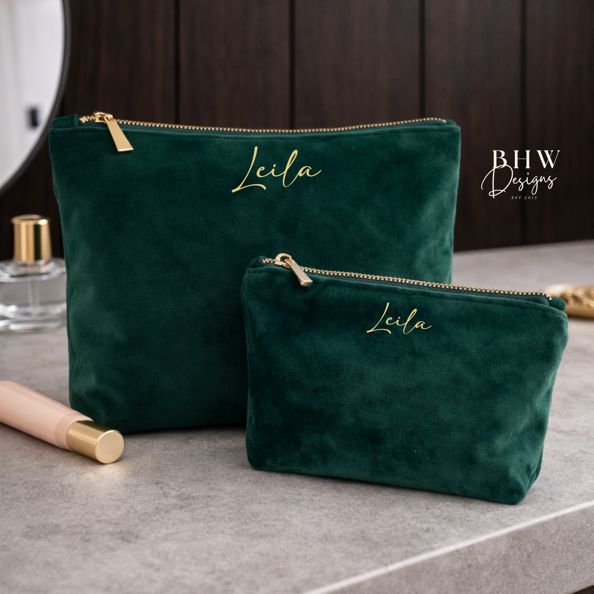 Two green velvet pouches with 'Leila' embroidered on them, placed on a gray surface.