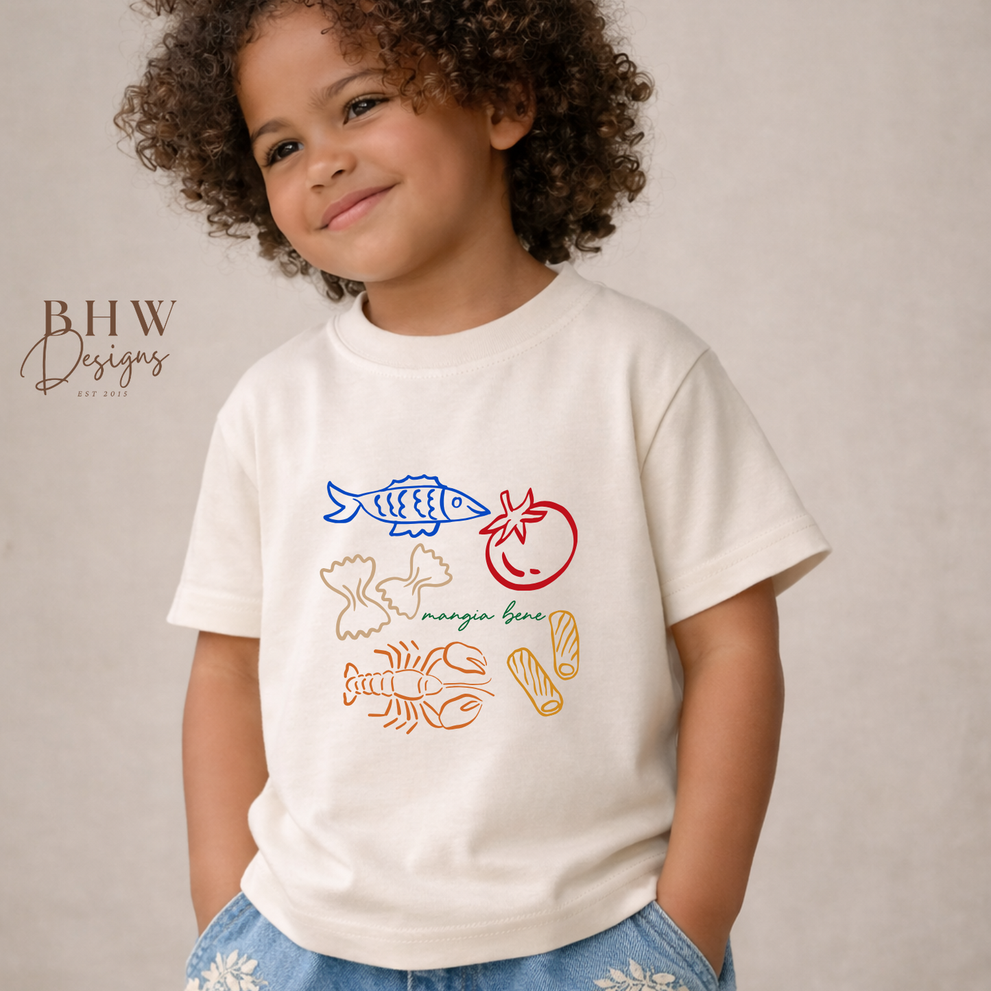 Child wearing a cream t-shirt with colorful graphics and text, standing against a plain background.