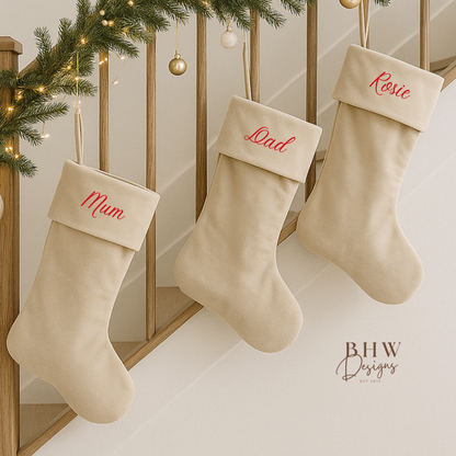 Three beige stockings with personalised names hanging on a staircase decorated with Christmas lights and garlands.