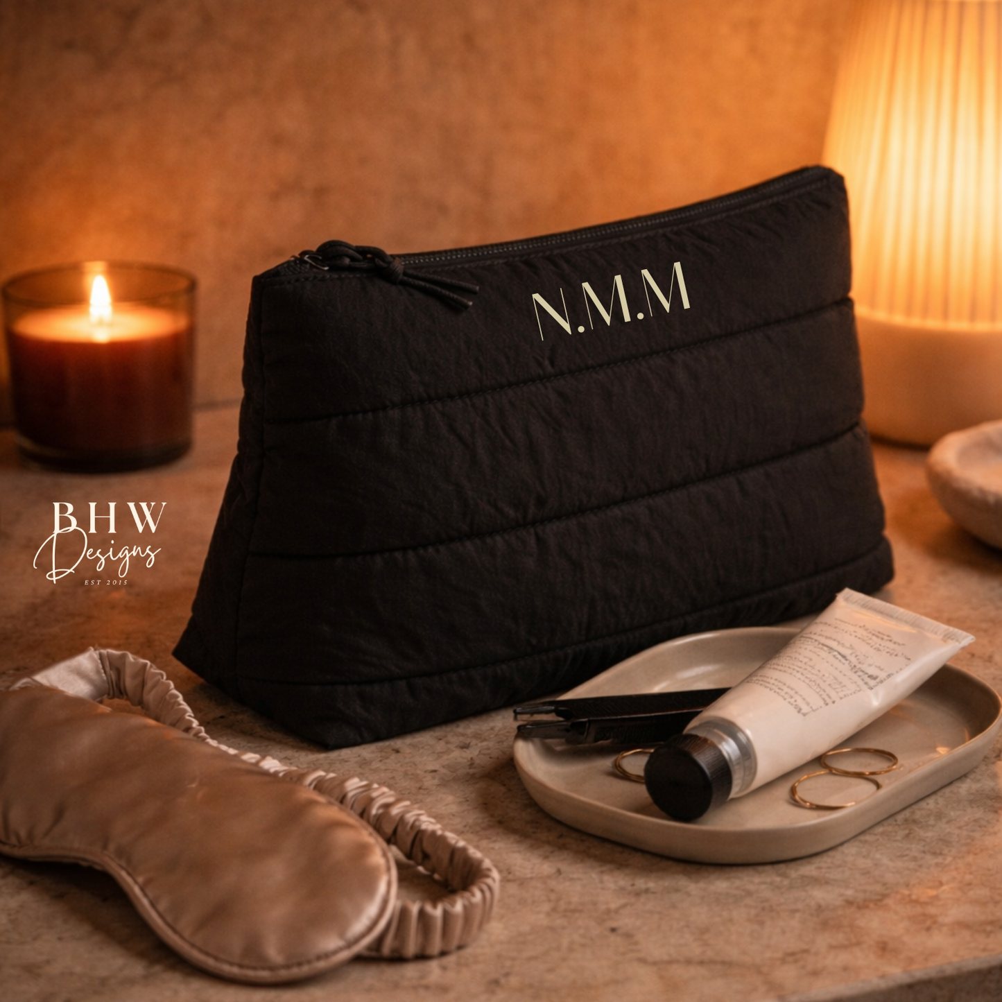 Black pouch with 'N.M.M' branding on a marble surface with skincare products and a candle.