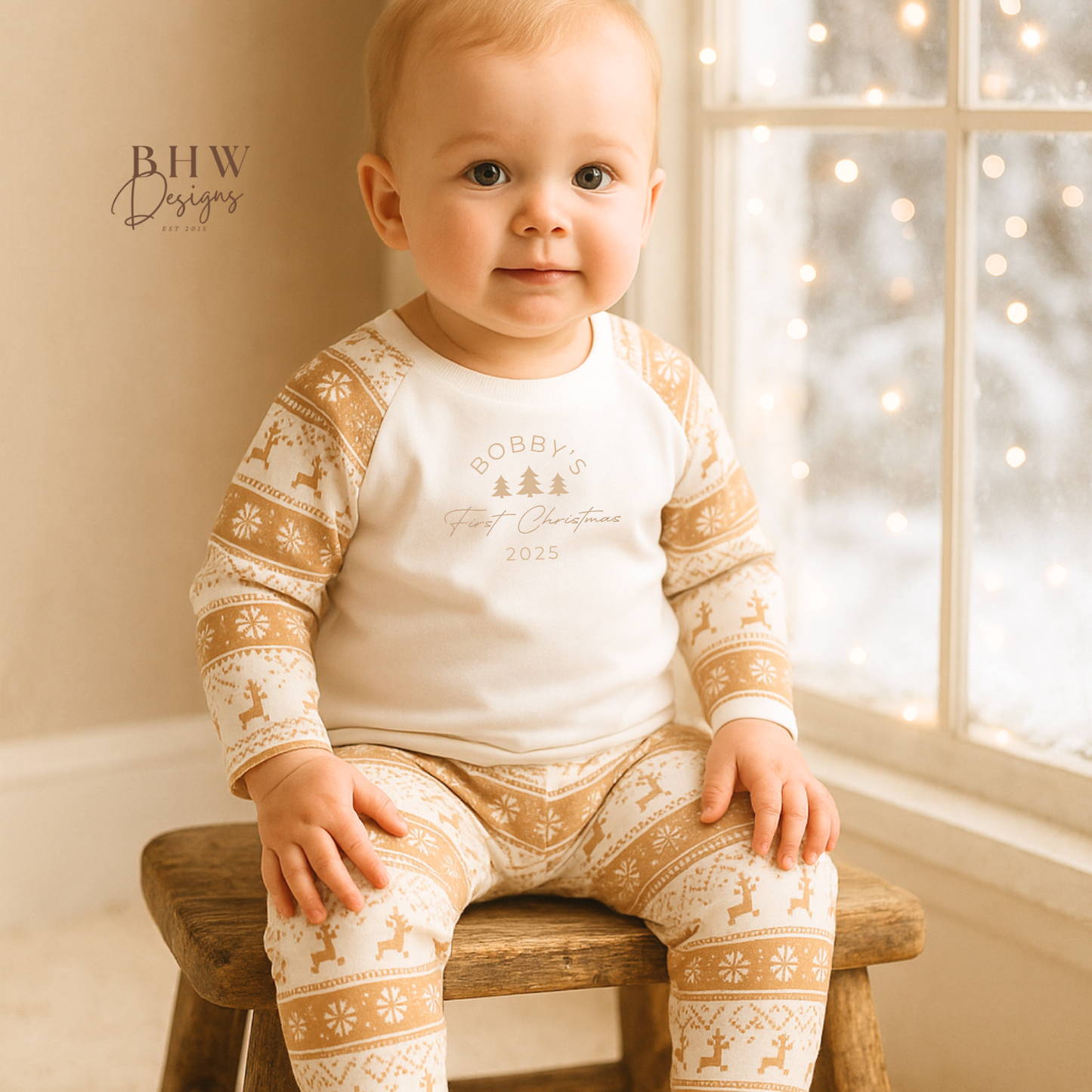 Baby wearing a white and beige fair isle pyjamas with a personalised first Christmas motif on the front.
