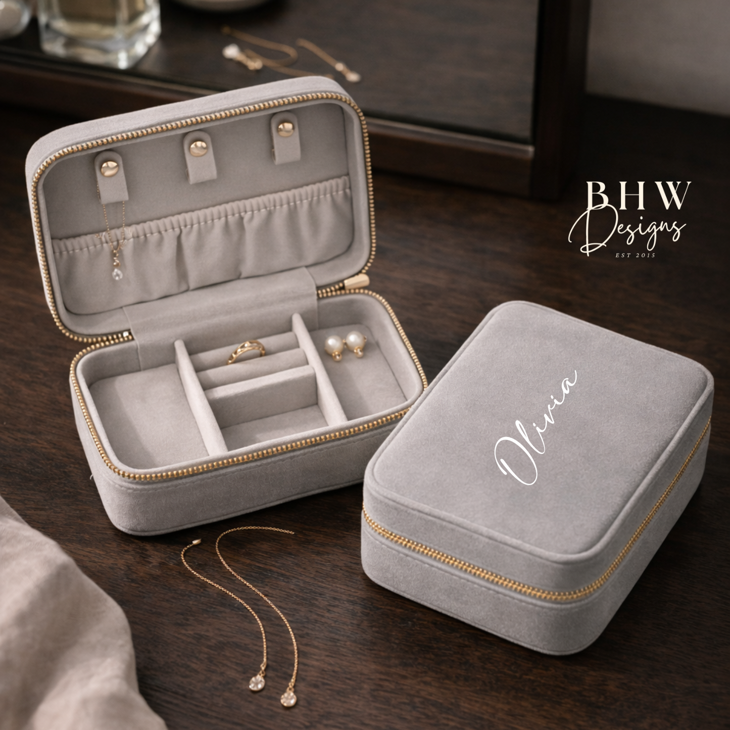 Grey velvet jewellery box with 'Olivia' on the top on a wooden surface, featuring jewellery inside.