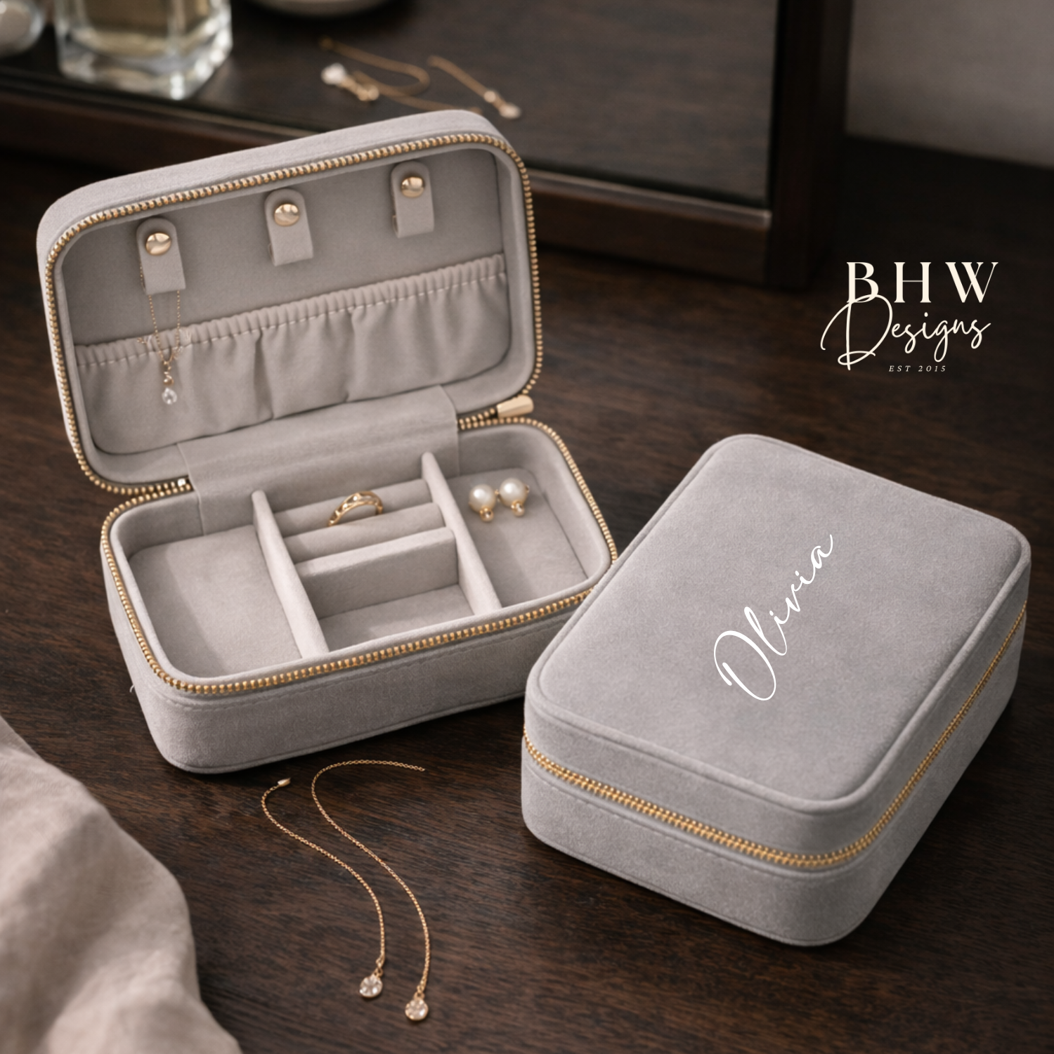 Grey velvet jewellery box with 'Olivia' on the top on a wooden surface, featuring jewellery inside.