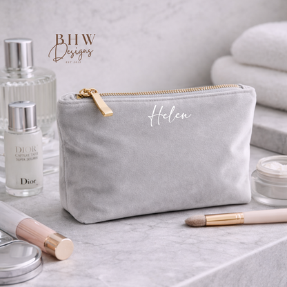 Gray makeup pouch with gold zipper on a marble surface with cosmetic products.