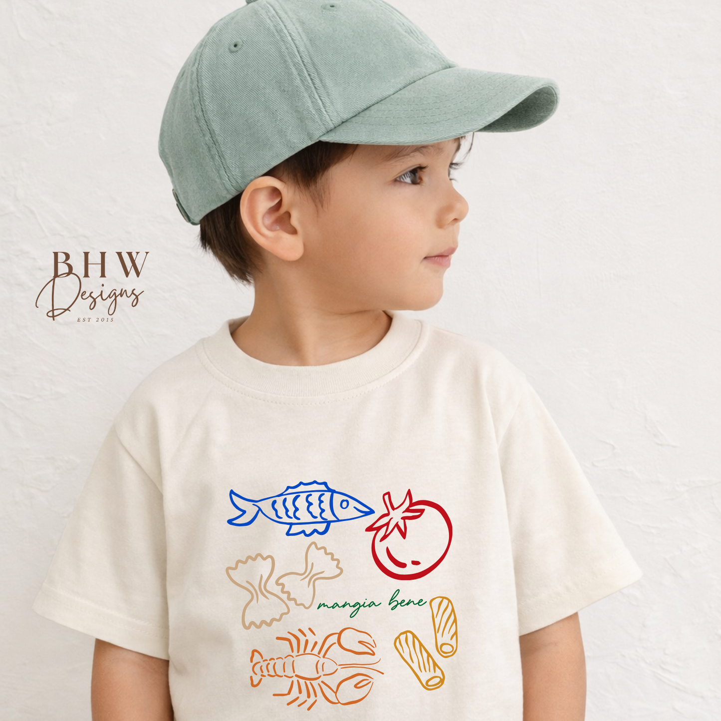 Child wearing  cream t-shirt with colourful food illustrations and a green cap on a light background.