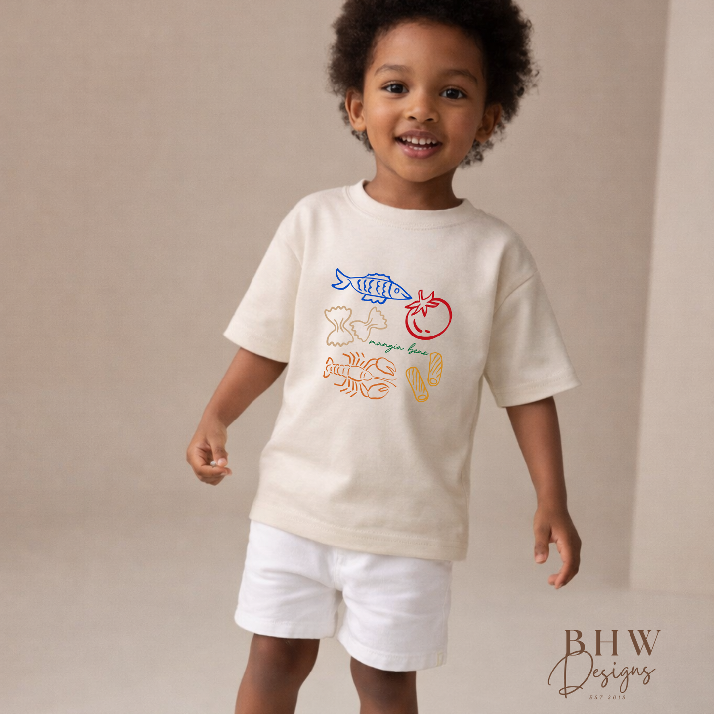 Child wearing a cream-colored t-shirt with colorful graphics and text, standing against a plain background.