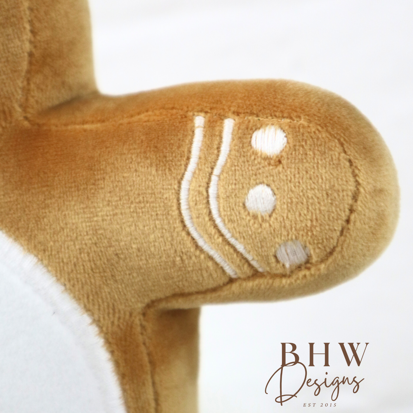 Close-up of a plush toy with a gingerbread man design on a white background, featuring the brand 'BHW Designs'.