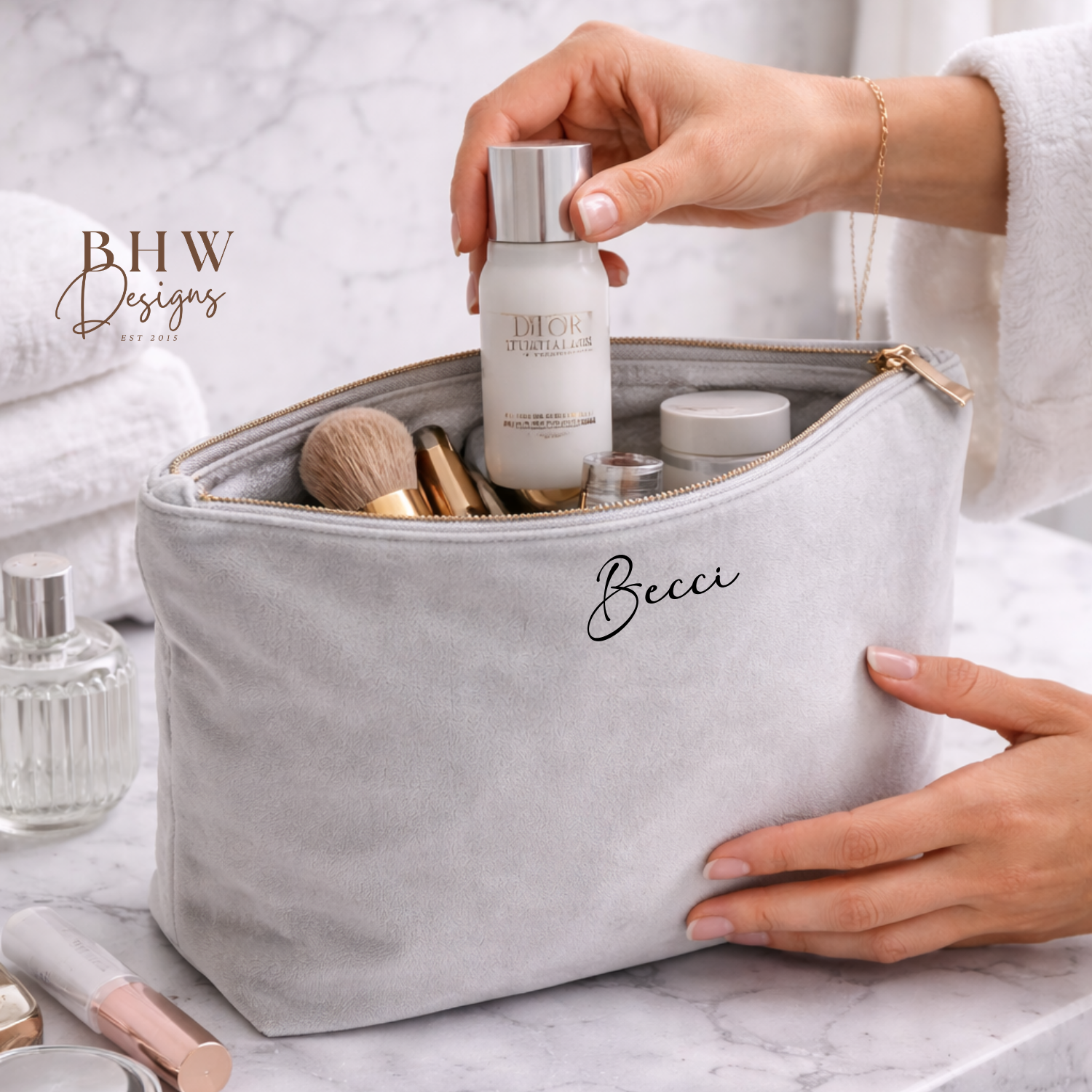 Person holding a makeup bag with skincare products on a marble surface, featuring BHW Designs branding.