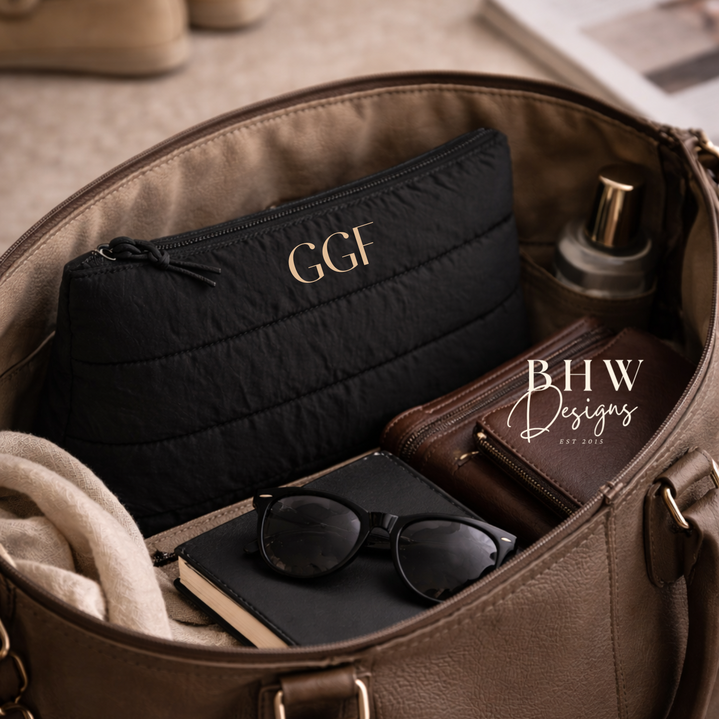 Open brown leather bag with black pouch, sunglasses, and other items on a beige surface. 