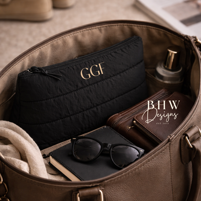 Open brown leather bag with black pouch, sunglasses, and other items on a beige surface. 