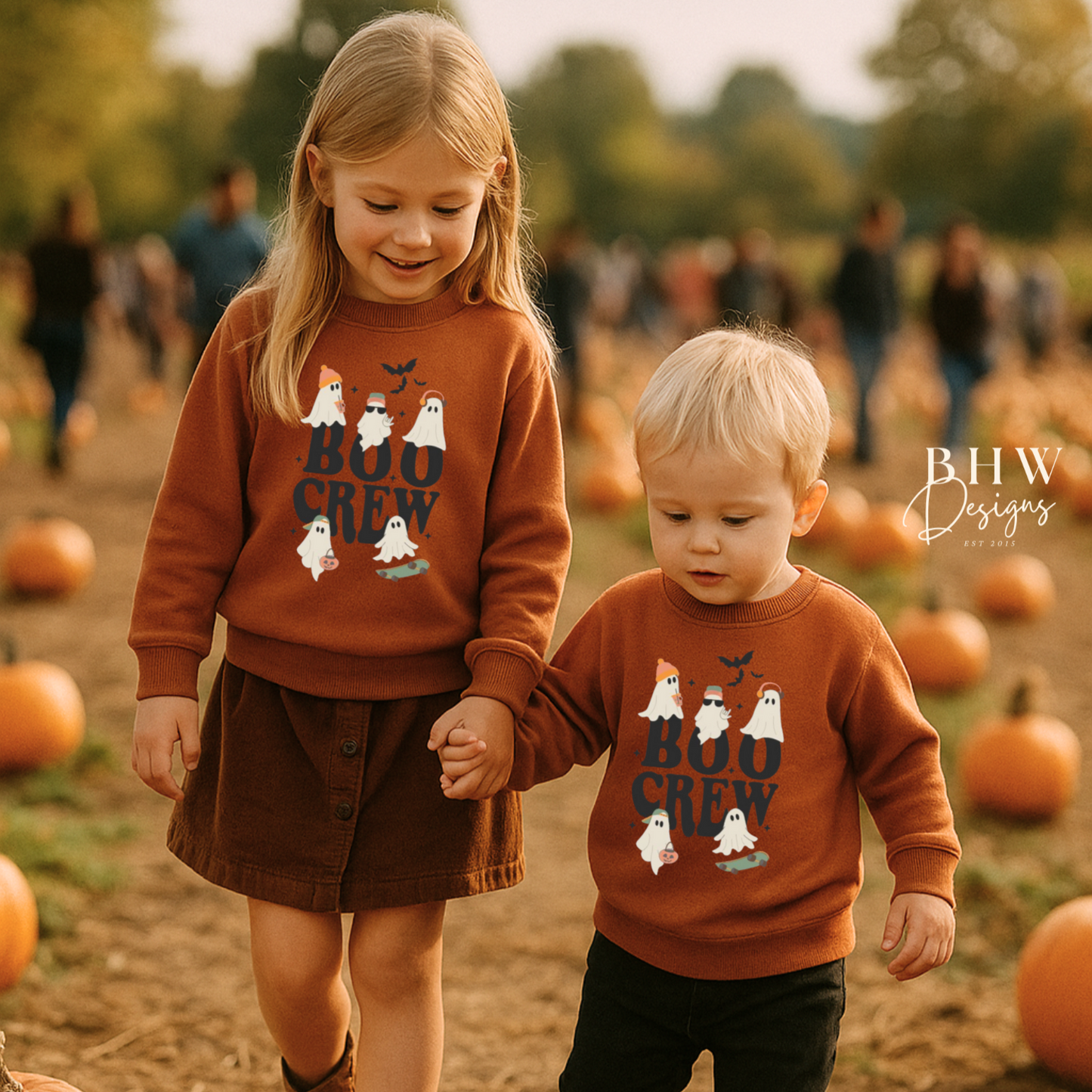 Two children in matching 'Boo Crew' rust orange colour sweatshirts walking through a pumpkin patch.
