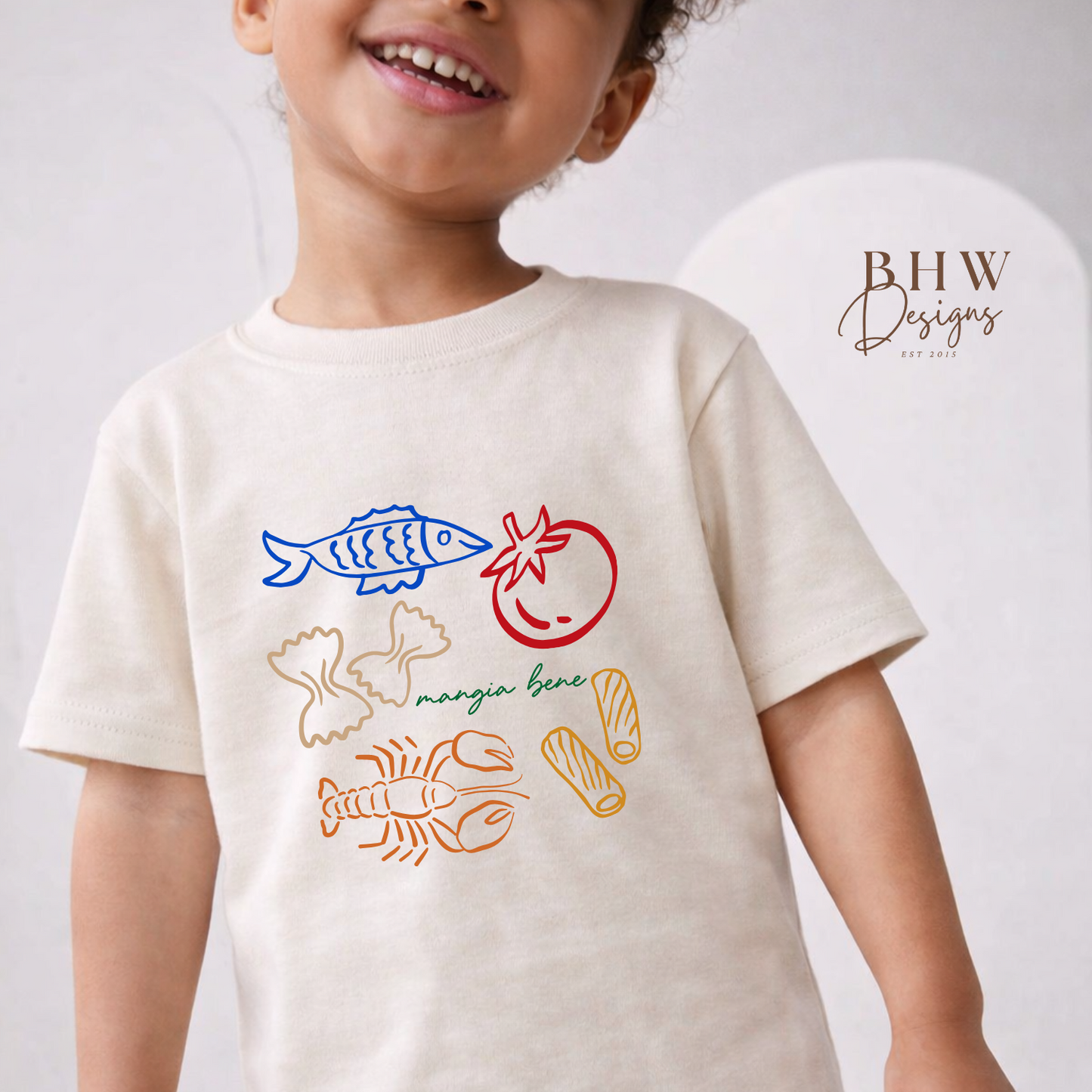 Child wearing a cream t-shirt with colourful graphics and text, standing against a plain background.