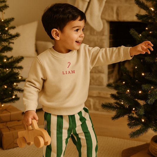 Child in a Christmas setting wearing a oat colour sweatshirt with a candy cane an Liam on the front in red
