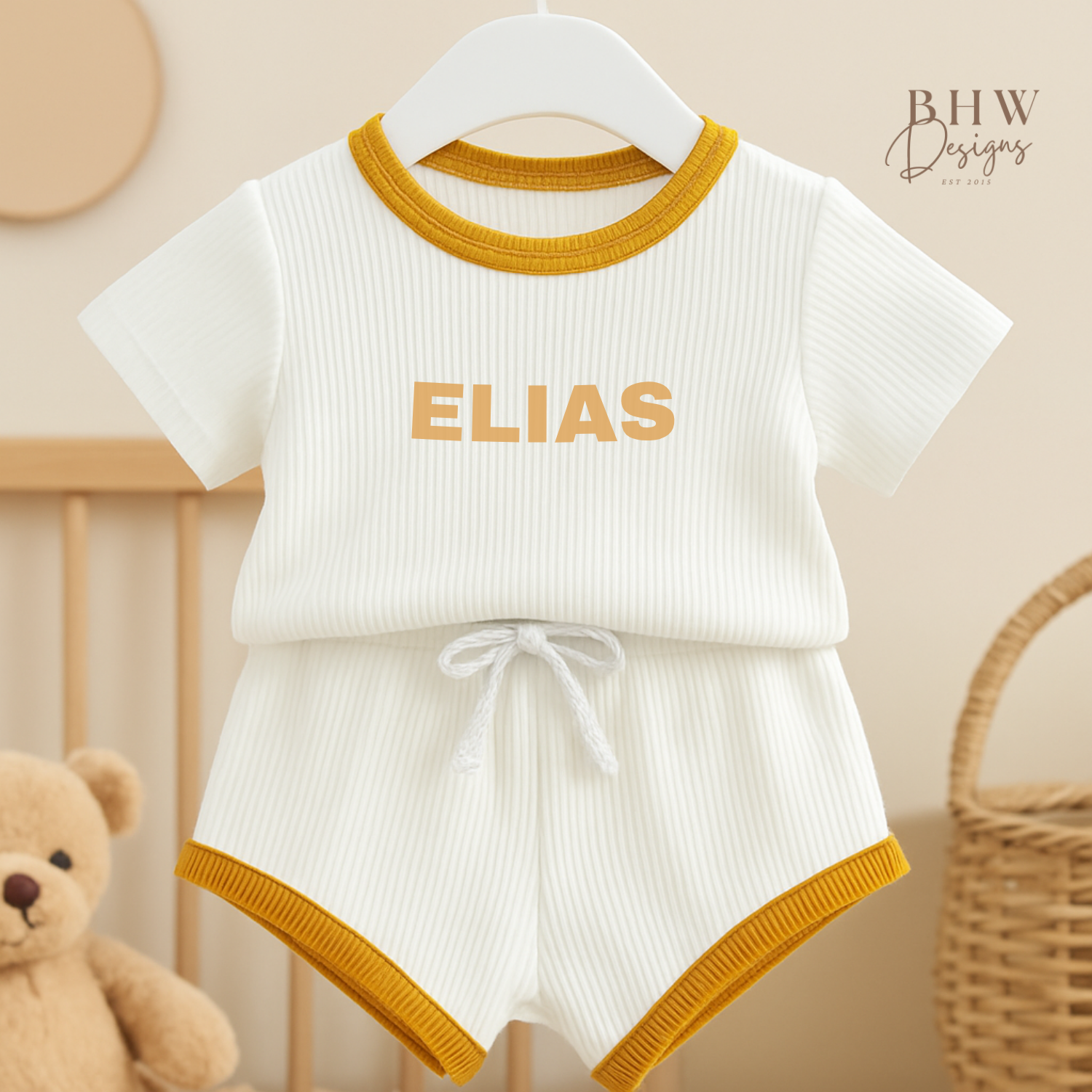 White baby ribbed outfit with mustard edge on a hanger, featuring the name 'ELIAS'.
