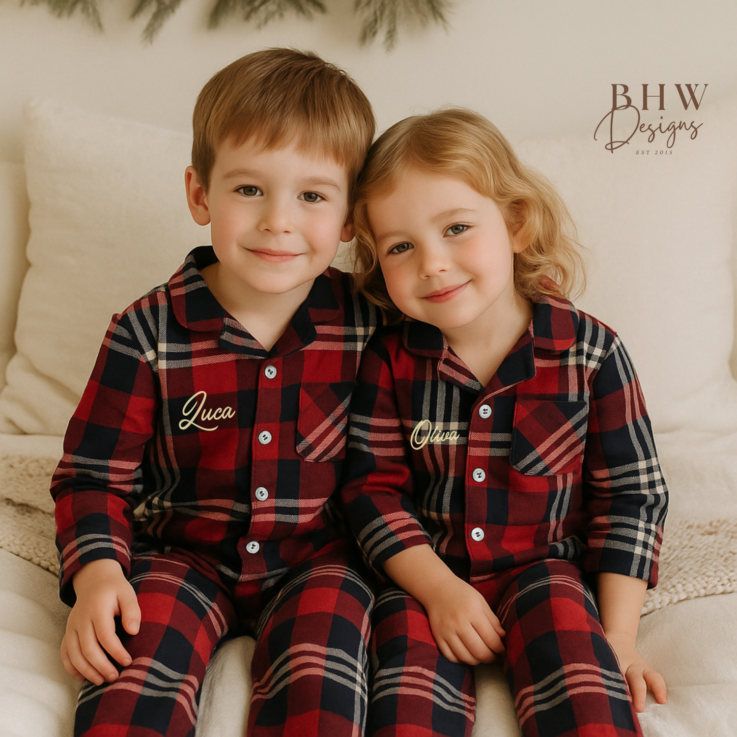 Two children wearing red and navy plaid pyjamas sitting on a couch.