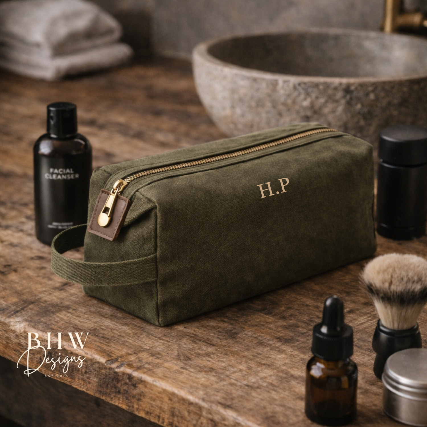 Olive green toiletry bag with initials on a wooden counter with grooming products.
