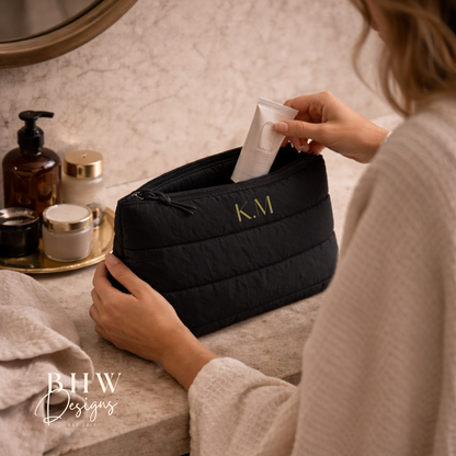 Person using a black cosmetic bag with initials 'K.M.' on a bathroom counter.