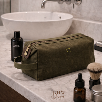 Olive green toiletry bag with initials on a bathroom counter with grooming products.