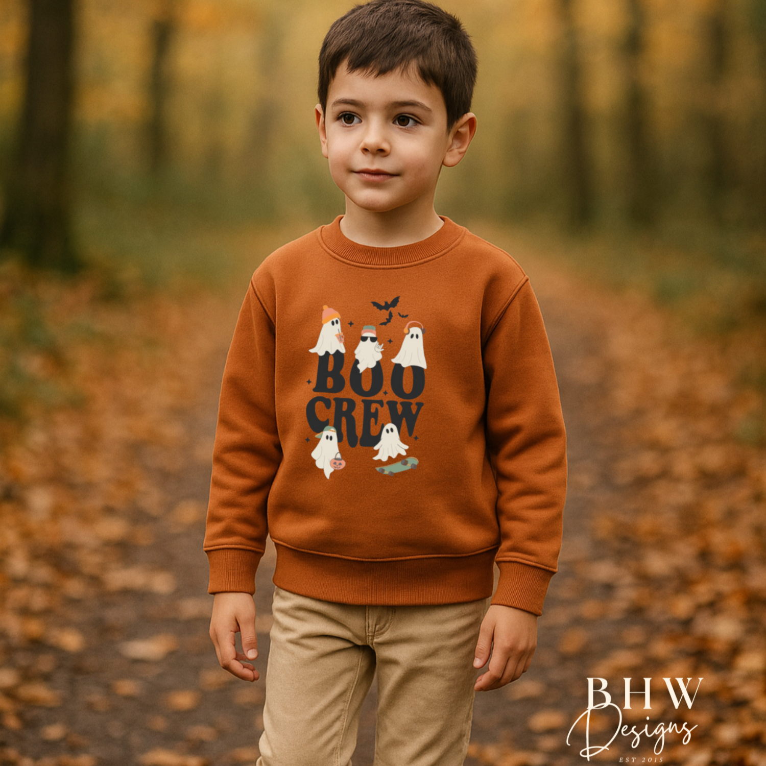 Child wearing a brown sweatshirt with 'BOO CREW' text and ghost graphics in an autumn forest.