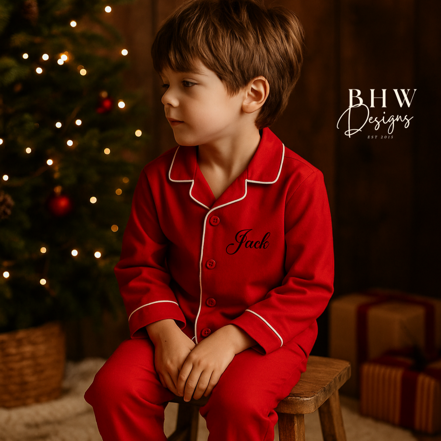Child in red personalised pyjamas sitting on a stool in front of a Christmas tree with presents.