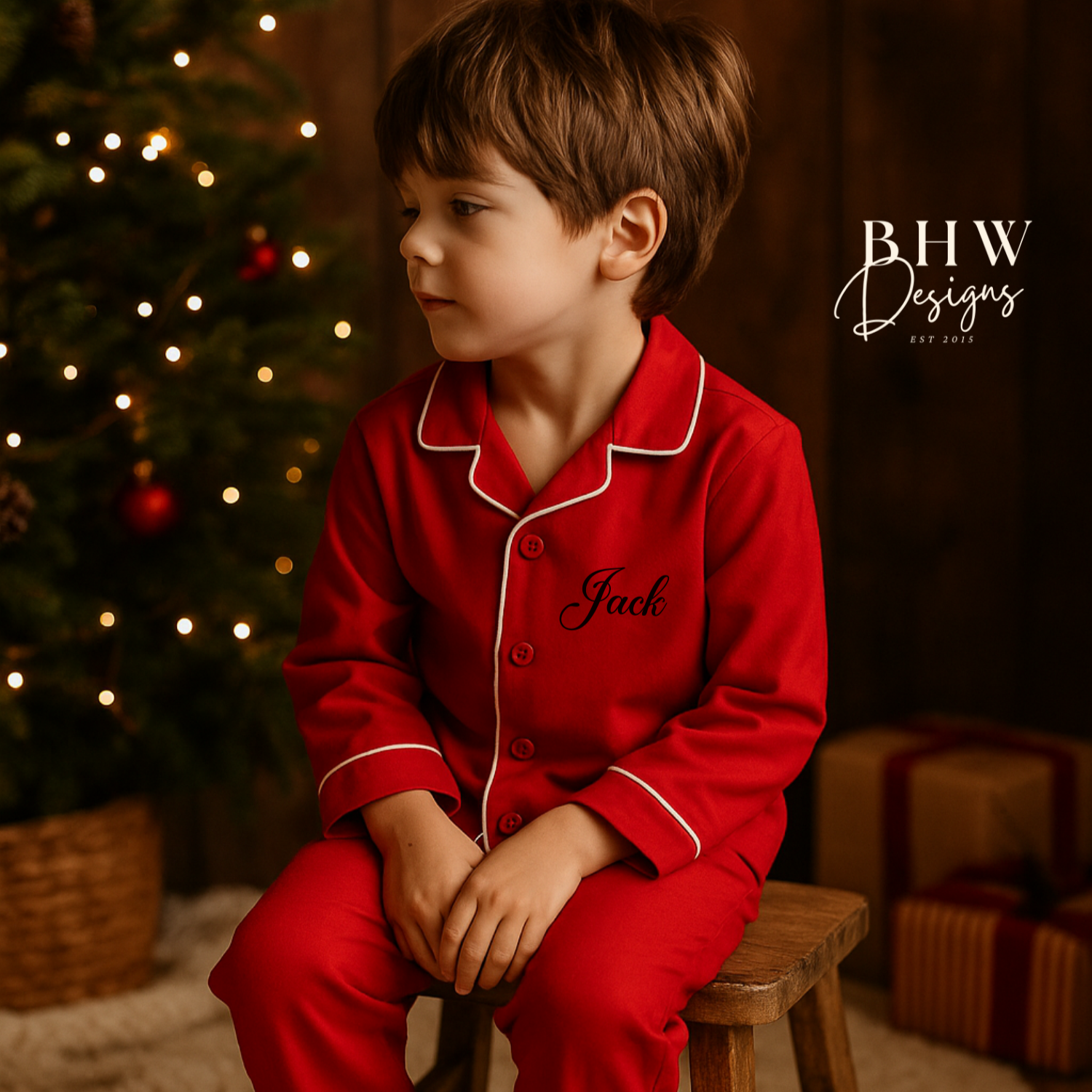 Child in red personalised pyjamas sitting on a stool in front of a Christmas tree with presents.