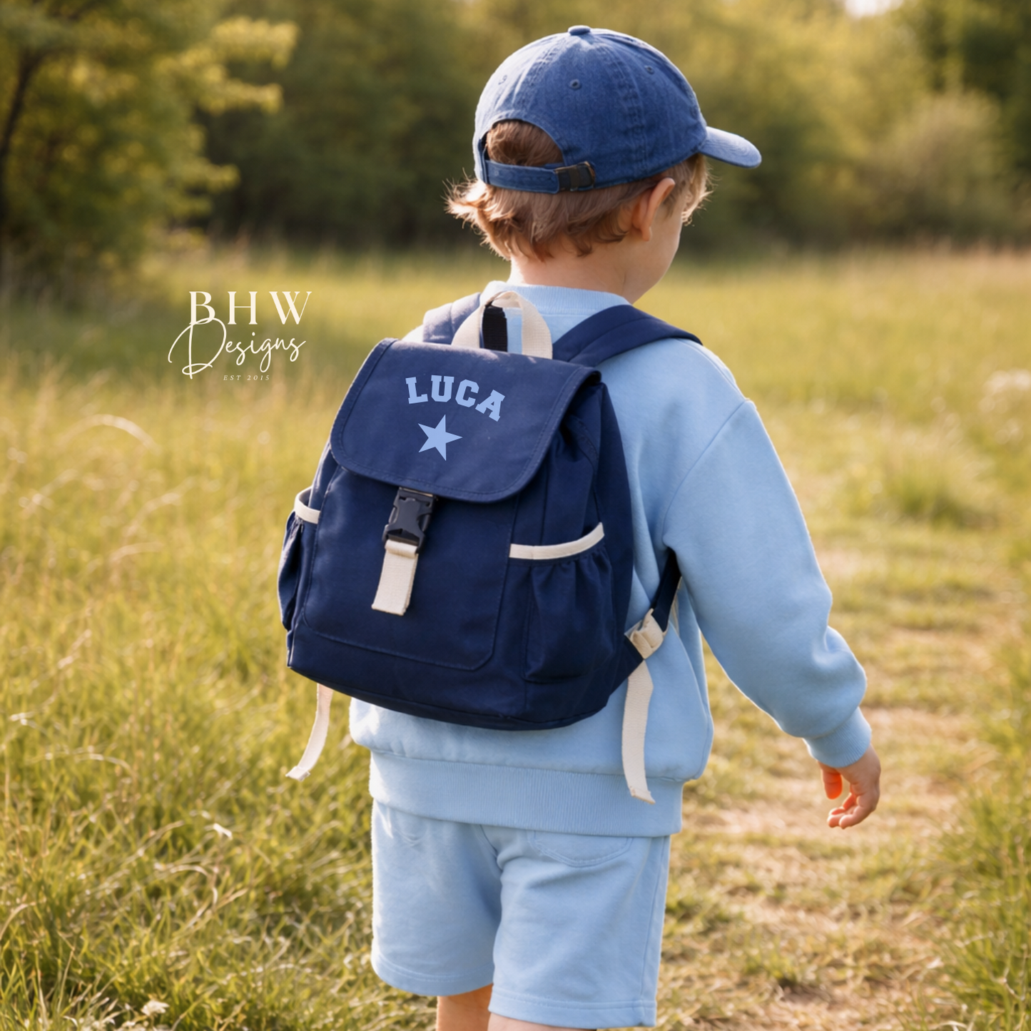 Child wearing a blue backpack with 'LUCA' on it, standing in a grassy field.