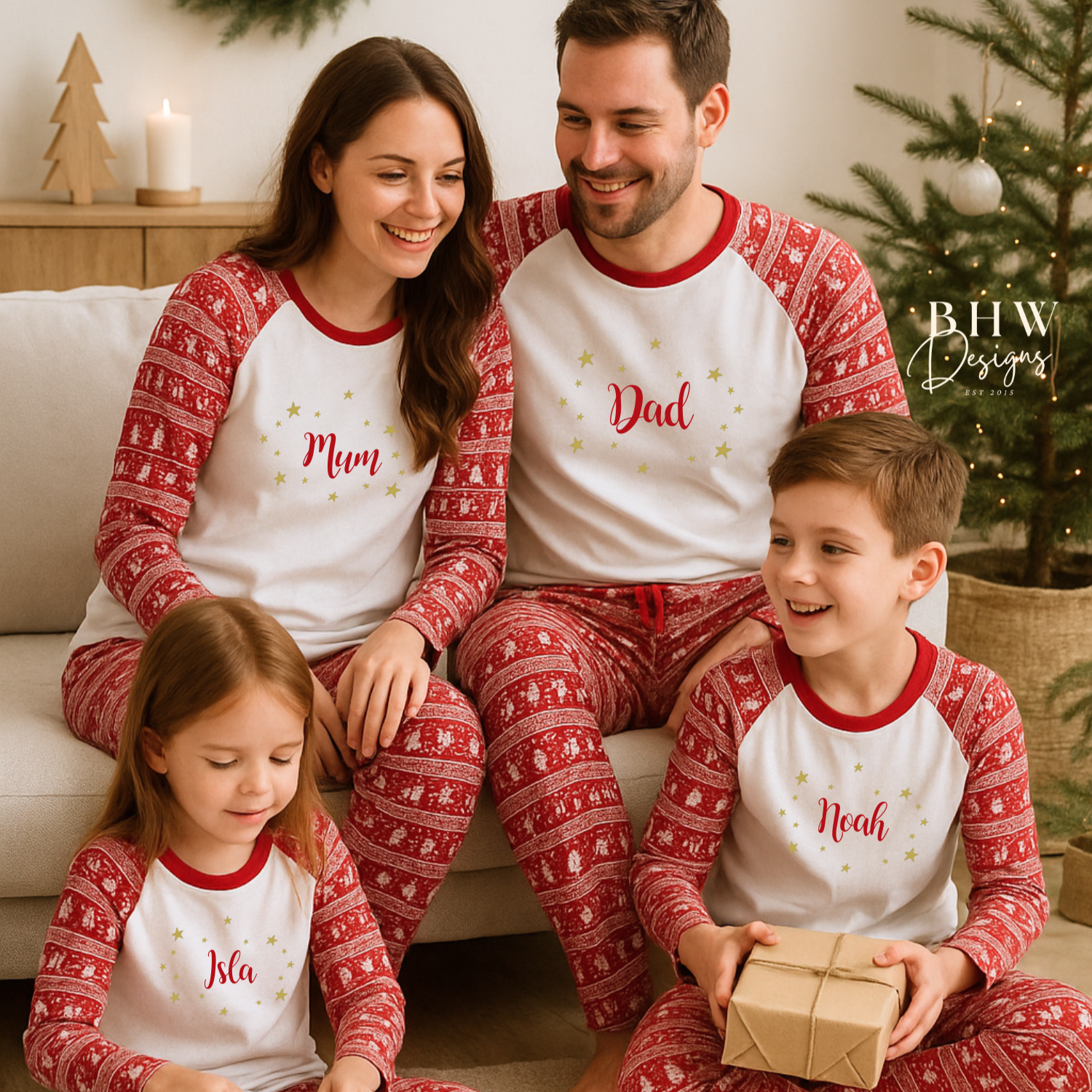 Family of four wearing matching personalised red and white fair isle print pyjamas in a festive setting with a Christmas tree.