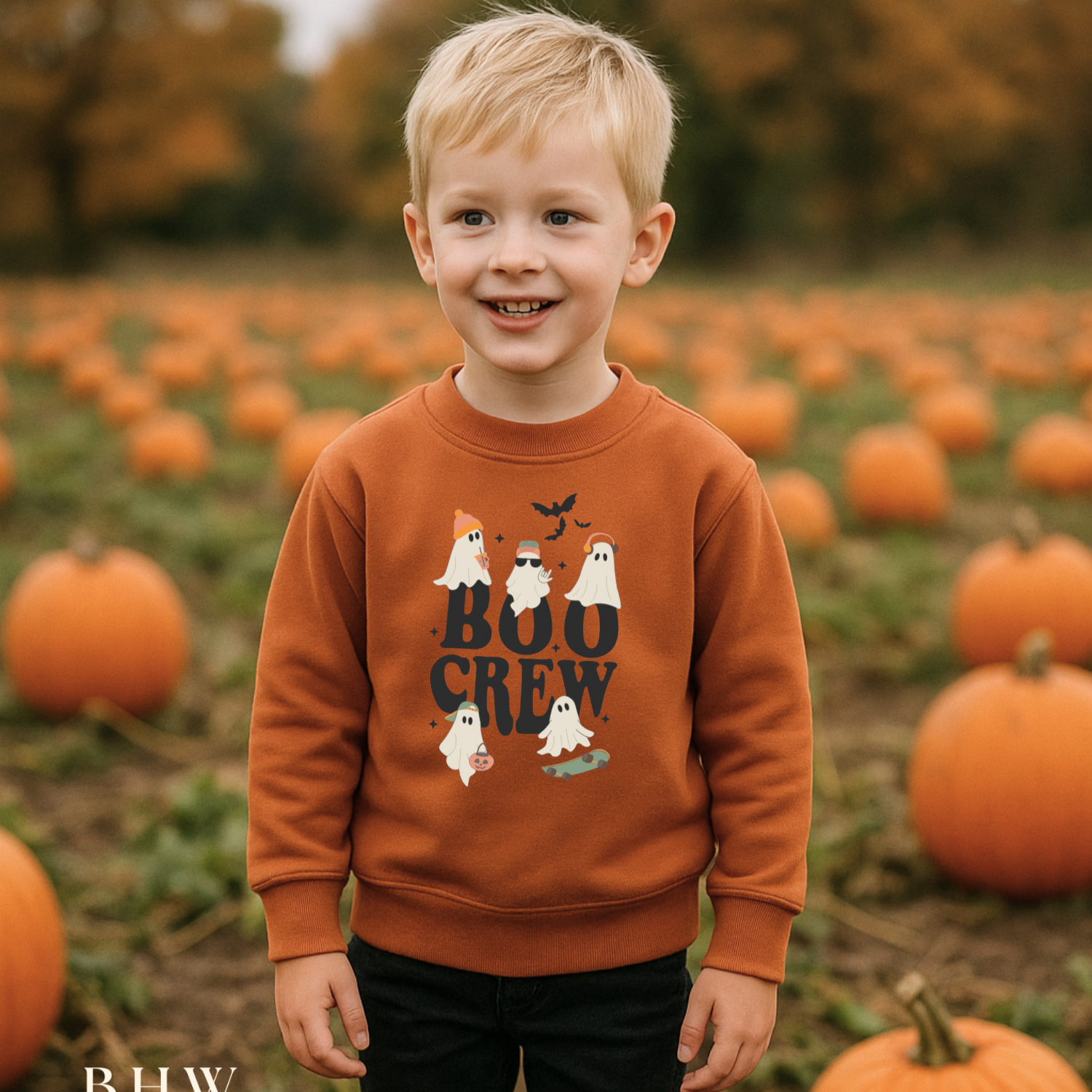Child wearing a 'Boo Crew' rust orange sweater in a pumpkin patch