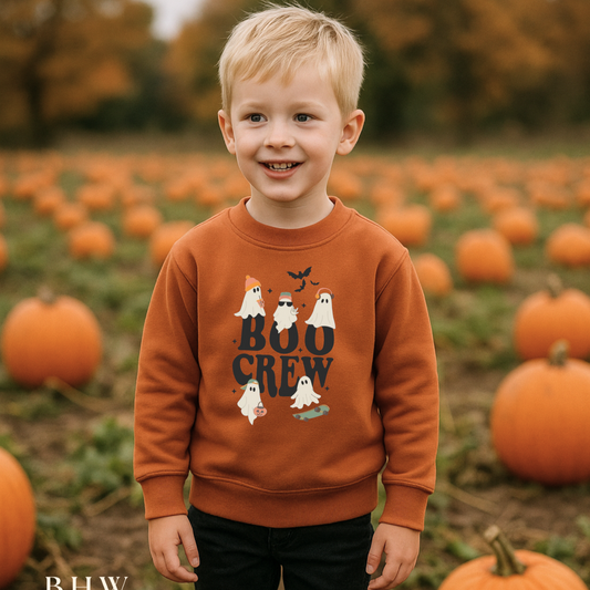 Child wearing a 'Boo Crew' rust orange sweater in a pumpkin patch
