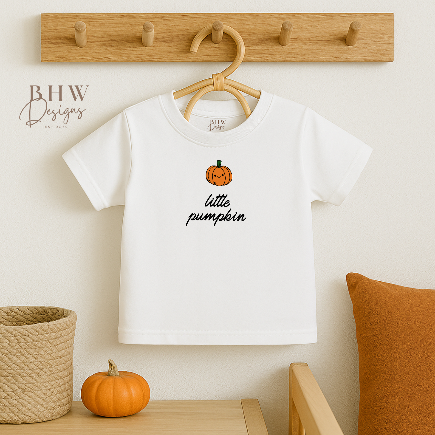 White t-shirt with 'little pumpkin' design on a hanger against a neutral wall.