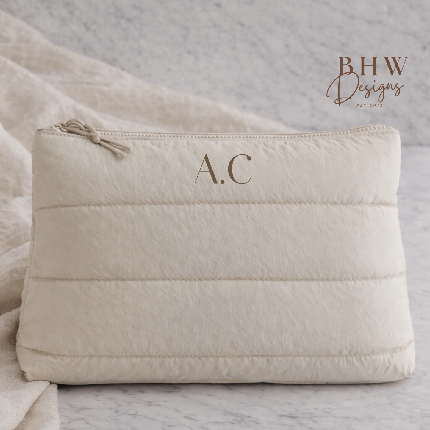 Beige quilted pouch with initials 'A.C.' on a marble surface, 