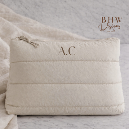 Beige quilted pouch with initials 'A.C.' on a marble surface, 