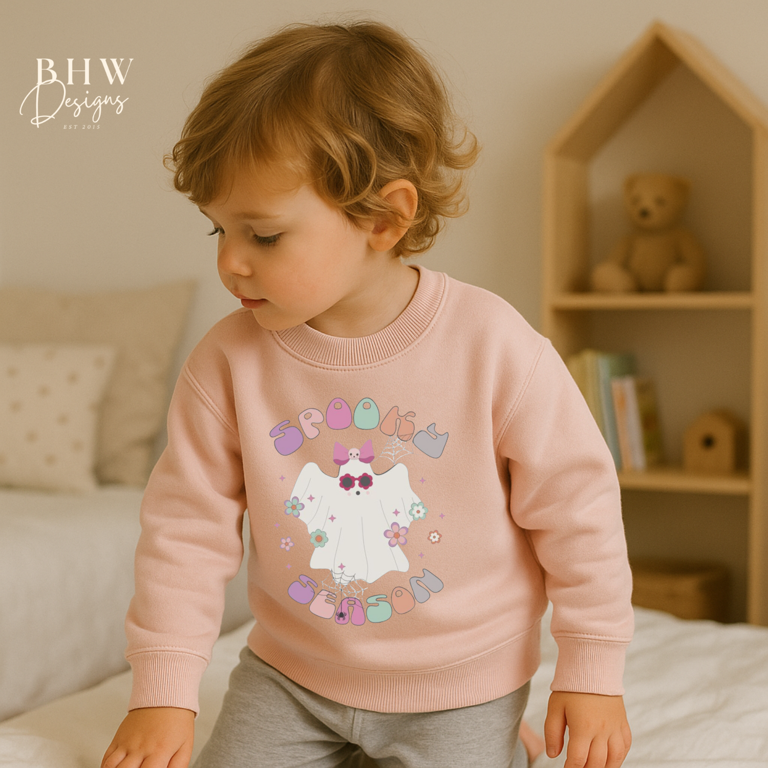 Child wearing a pink sweatshirt with spooky season ghost design on the front 
