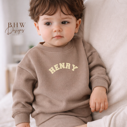 Child wearing a taupe waffle  sweatshirt with 'HENRY' printed in cream