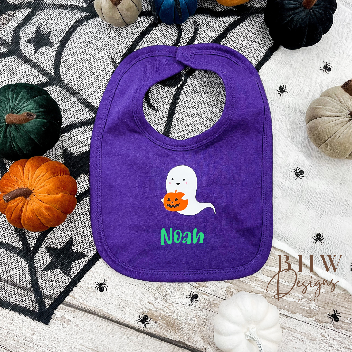 personalised Purple bib with ghost design and 'Noah' text on a Halloween-themed background with pumpkins and spider webs