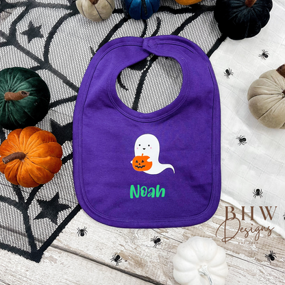 personalised Purple bib with ghost design and 'Noah' text on a Halloween-themed background with pumpkins and spider webs