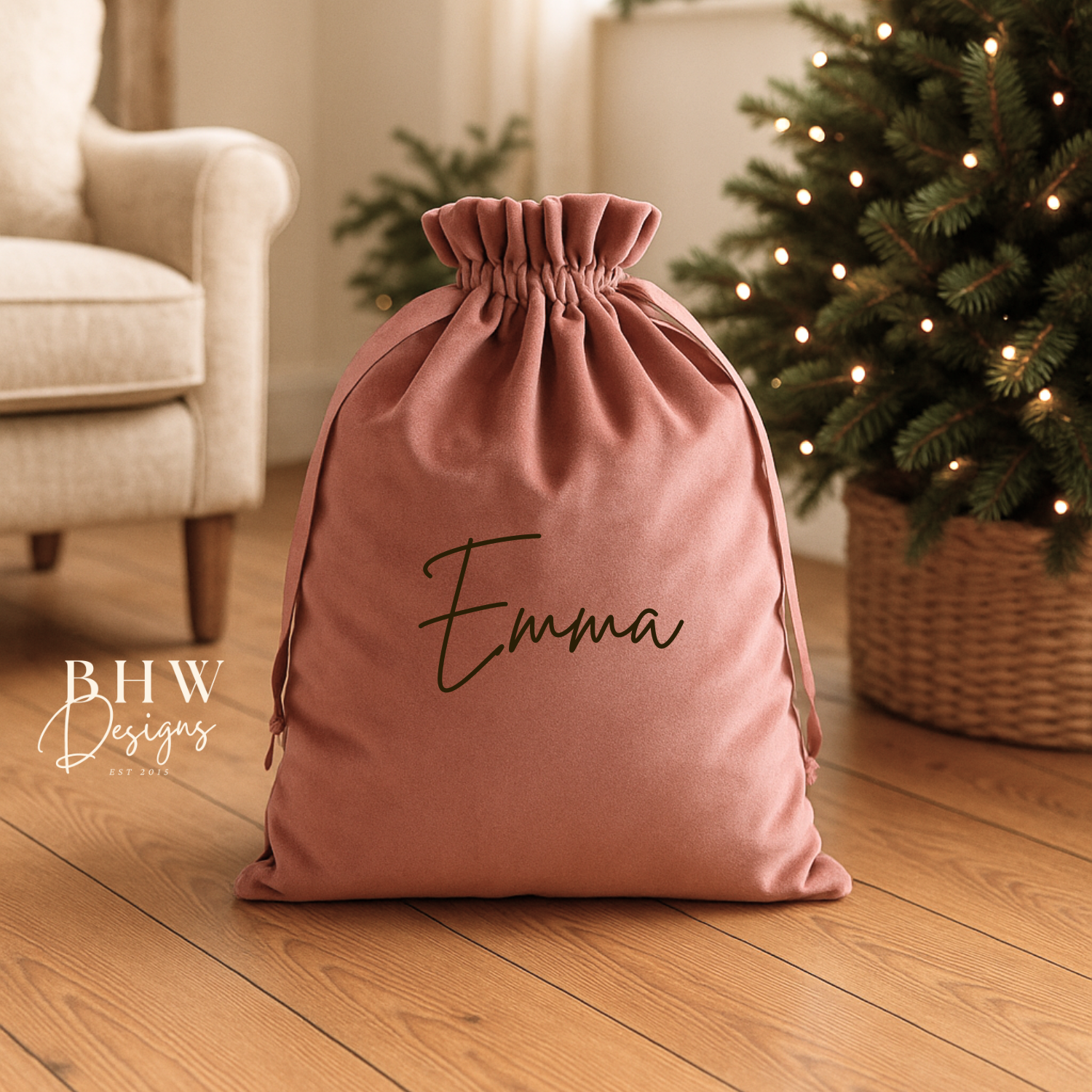 Pink drawstring bag with 'Emma' written on it, placed on a wooden floor with a Christmas tree in the background.