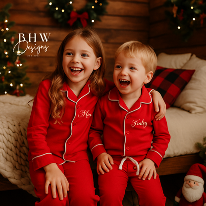 Two children in red pyjamas with  names printed on, sitting on a bed in a festive room.
