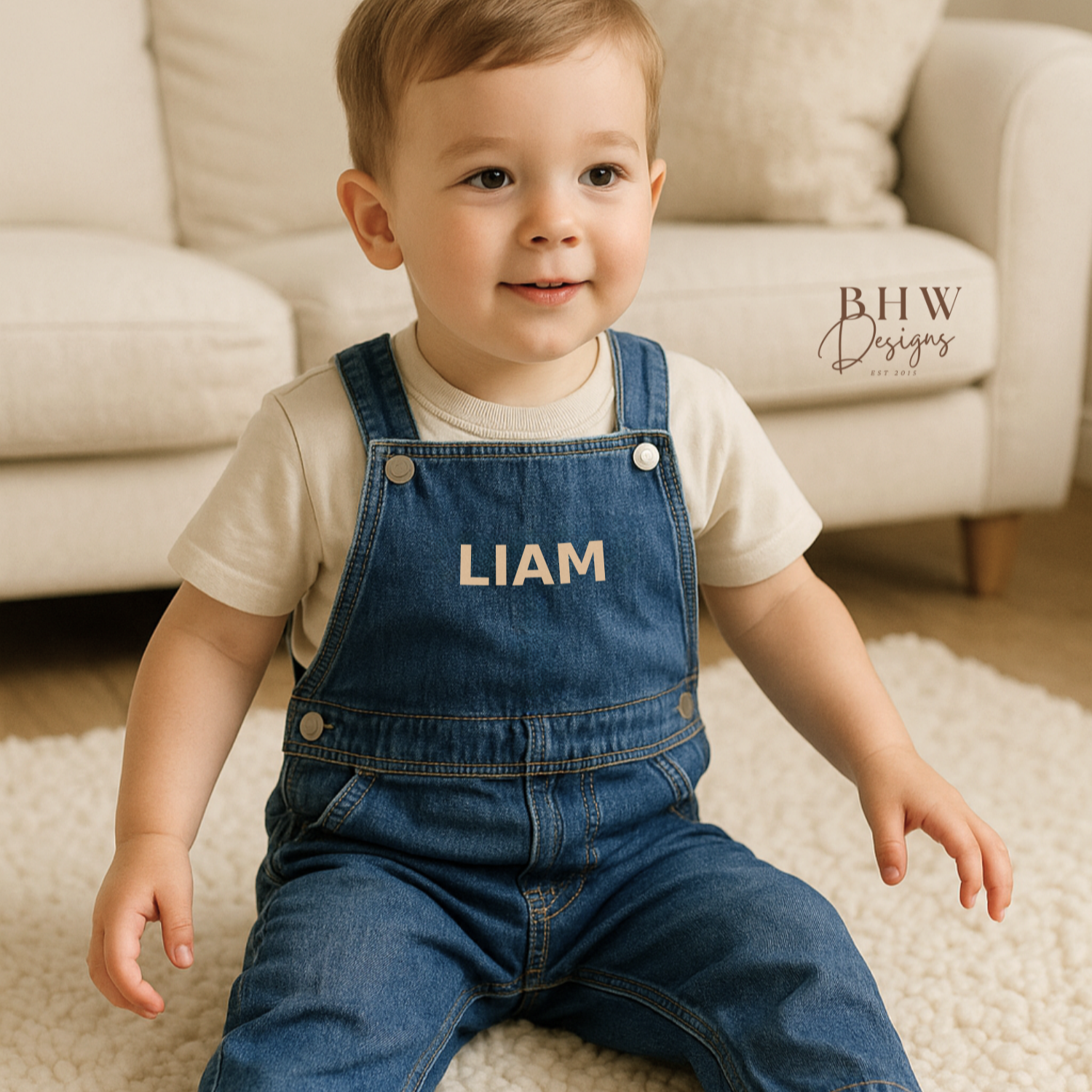 Child wearing blue denim overalls with 'LIAM', sitting on a carpeted floor.