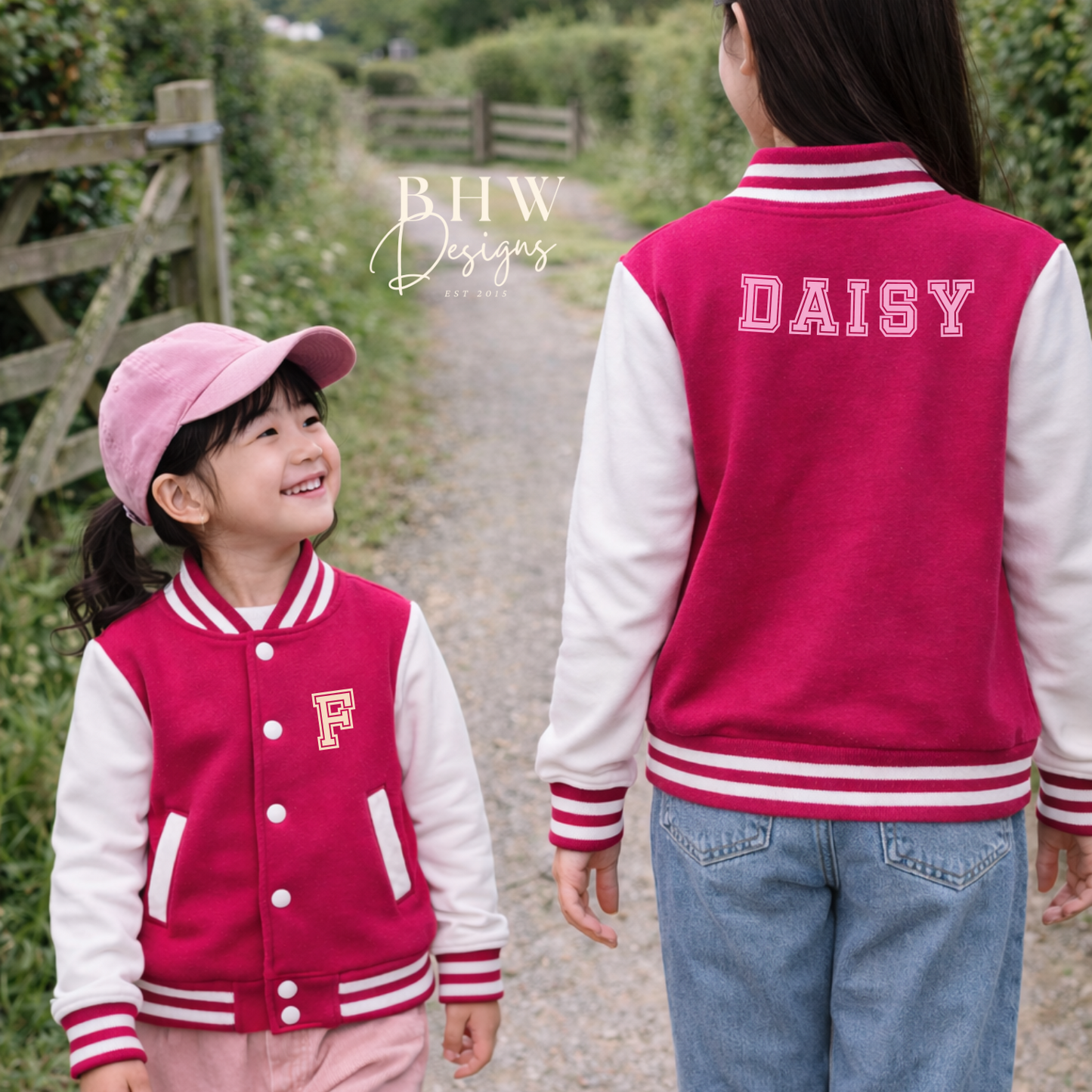 Two children wearing matching pink and white letterman jackets with 'DAISY' and 'F' on a path.