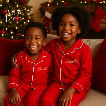 Two children in red pyjamas with names on them, sitting on a couch in a festive setting.