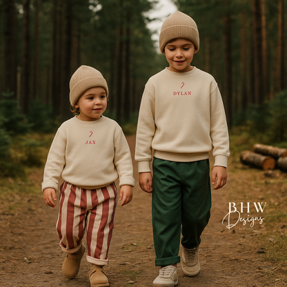 Two children in a forest wearing wearing oat colour sweatshirt with a candy cane and Jax and Dylan on the front in red